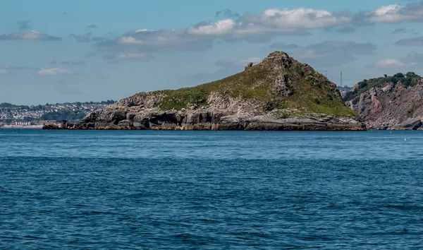 A green-topped rocky island just off a headland in calm blue sea